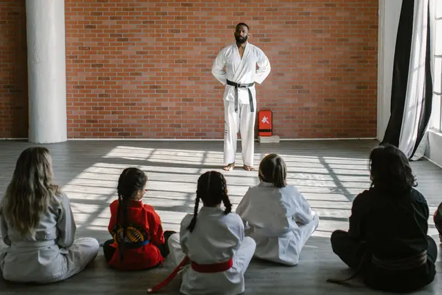 Clase de artes marciales en un dojo luminoso: el instructor frente al grupo, sentado en el suelo